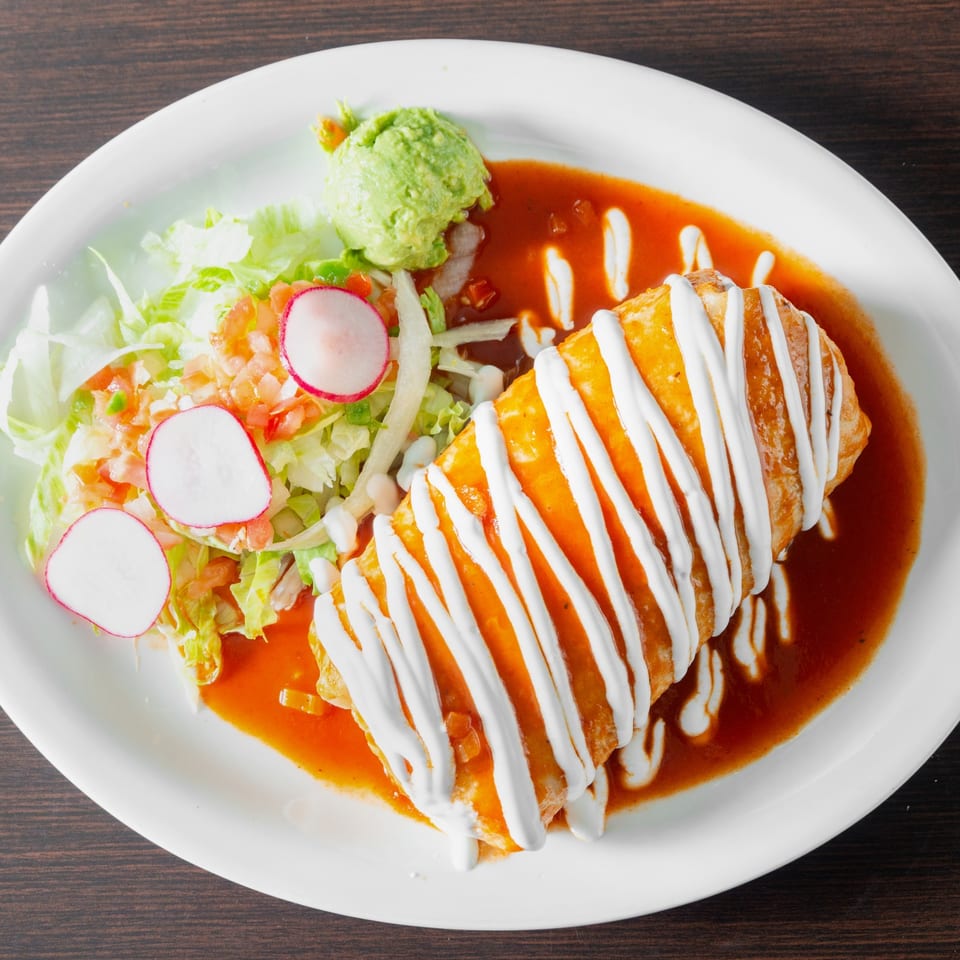 Sauced fried burrito with sour cream, guacamole and salad.