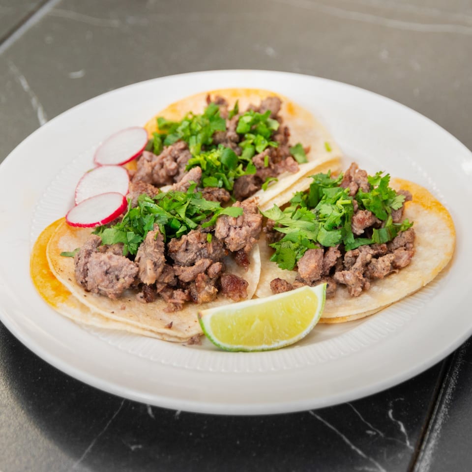 Three tacos with cilantro, radish and lime.